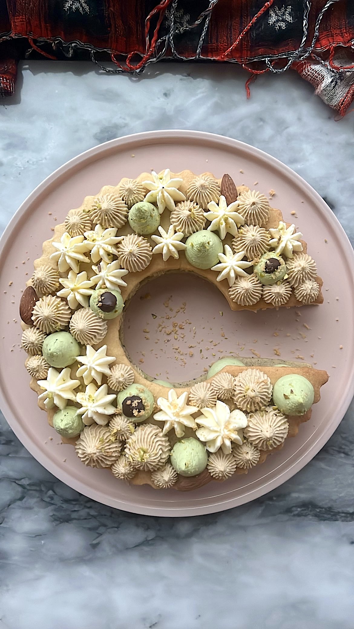 Birthday cake featuring a cookie shaped like the letter 'C' and decorated with variously shaped cream piping on top and between the layers